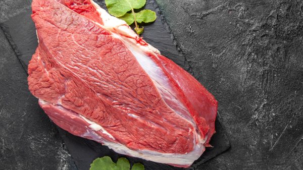 Top view of raw fresh red meat and leaves on cutting board on the right side on green black mix colors background