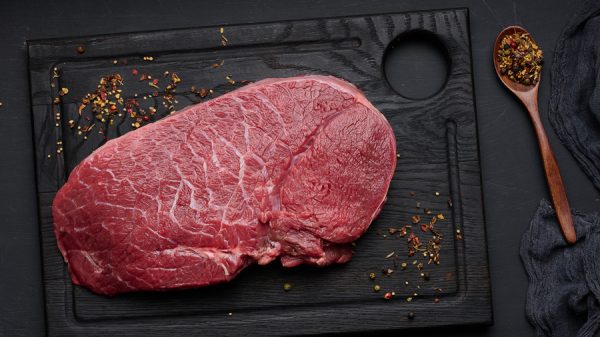 Raw beef tenderloin lies on a wooden cutting board on a black table, top view